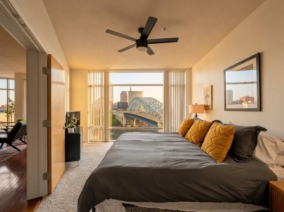 Bedroom with a dark bedspread, yellow cushions and a ceiling fan